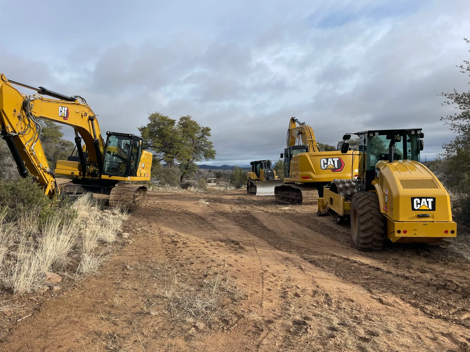 DB Excavation's fleet of CAT excavators, dozer, and compactor staged on a graded site near Prescott