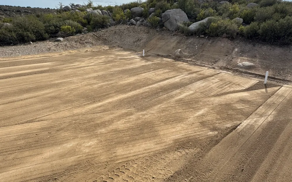 Compacted building pad cut into a granite slope with survey stakes near Prescott